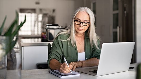 Older woman sitting on table with her laptop taking notes